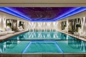 Awesome-indoor-pool-designs-with-cool-blue-ceiling-lighting-and-stylish-white-lounge-chair-also-large-enclosed-pool